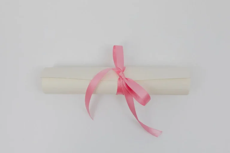 Rolled certificate tied with a pink ribbon on a plain background
