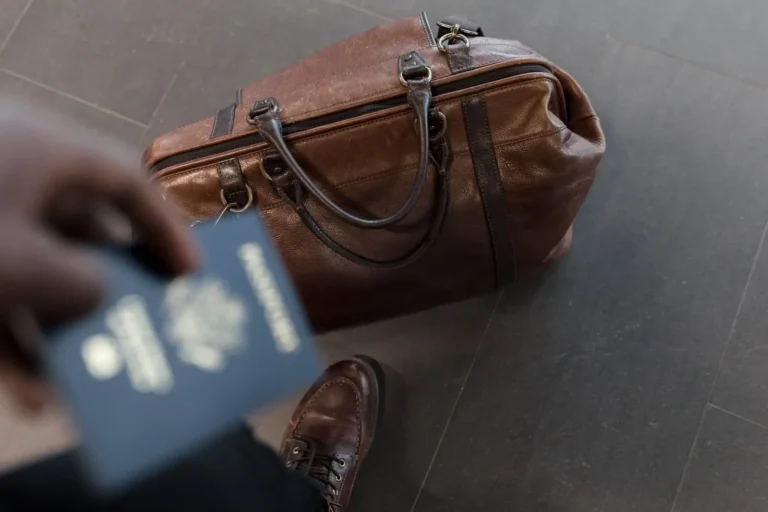 Hand holding a passport next to a leather travel bag