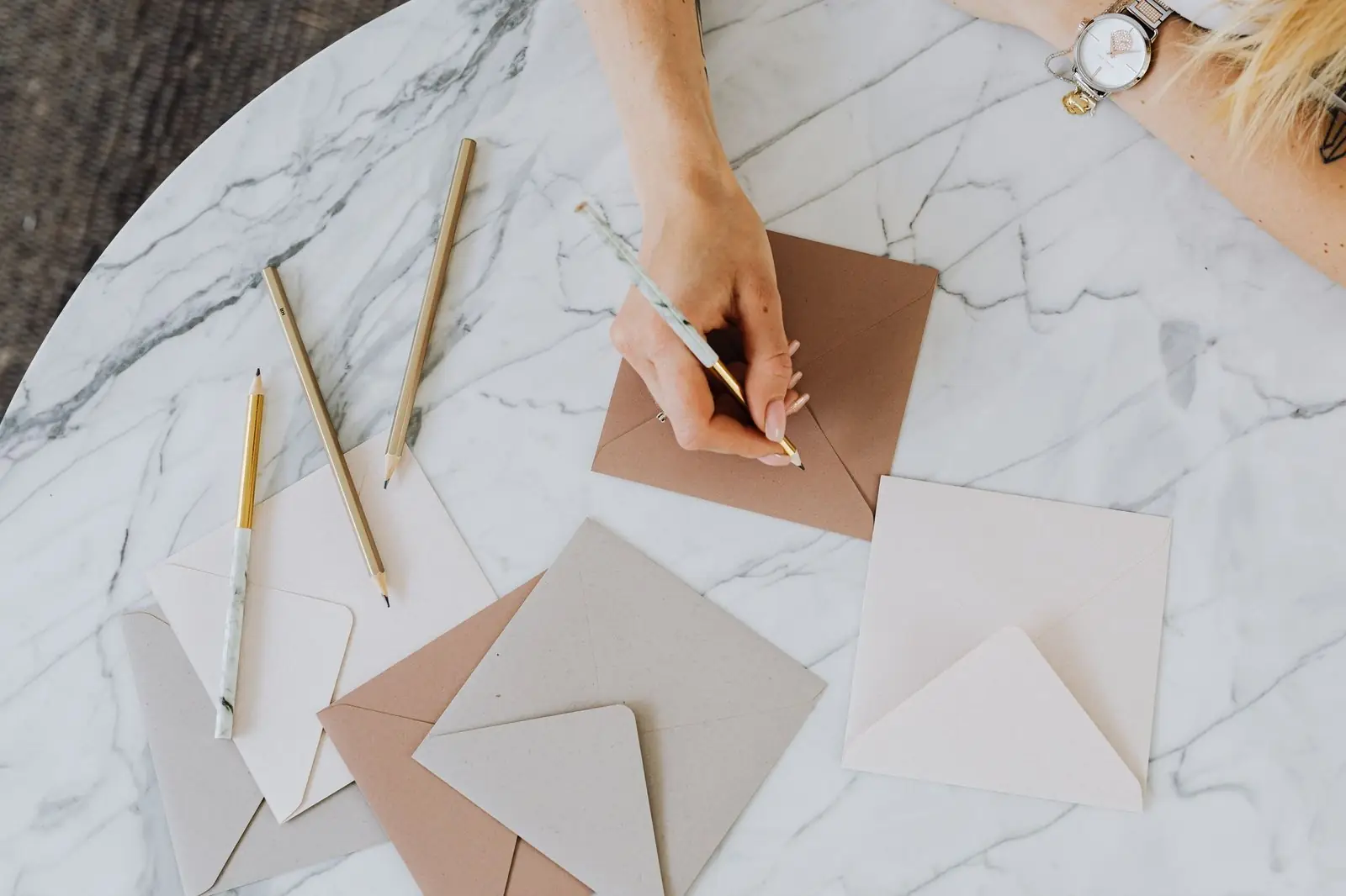 Hand addressing an envelope among blank envelopes on a marble table