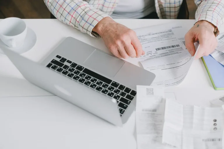 Person checking a printed receipt beside a laptop