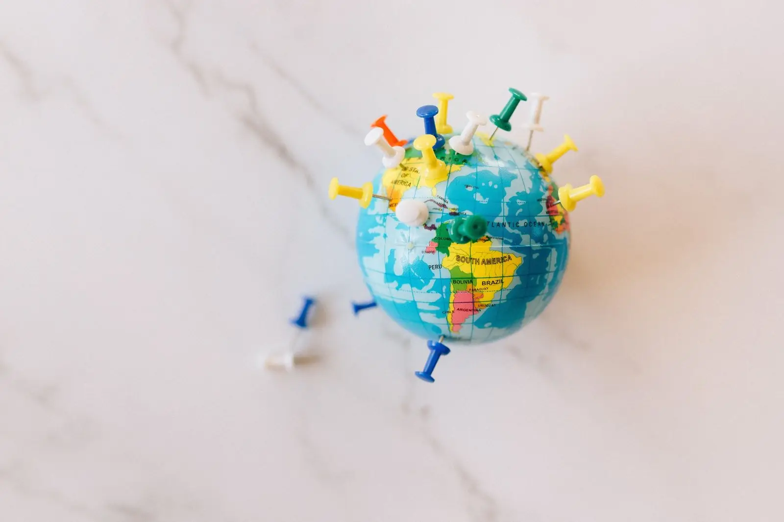 Small globe covered in map pins on a marble surface
