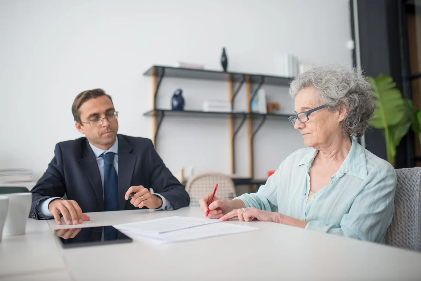 A professional going through papers at a table with an older woman who is signing
